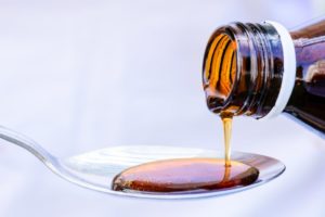 person pouring cough syrup onto a spoon